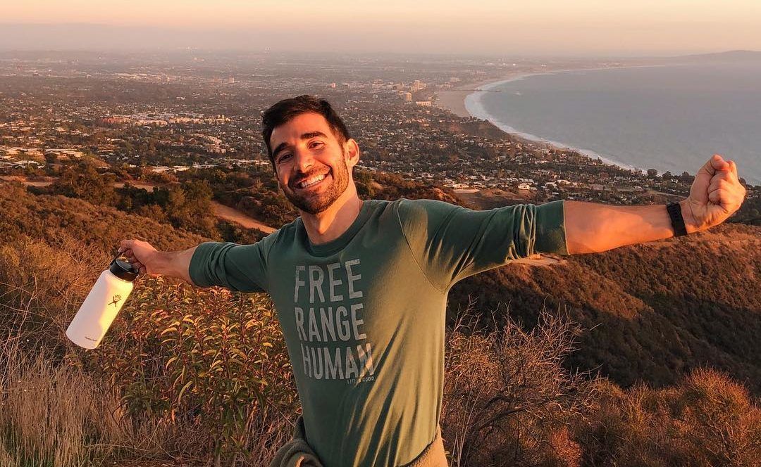 thedavecoastfreerange young man celebrating at the top of a mountain